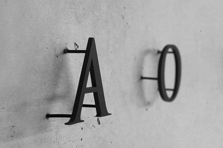 black aluminium letters A and O on a wall with distance holders