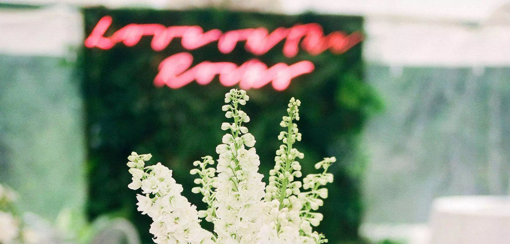 close-up of a white flower bouquet on a table at a wedding reception with a blurry red neon sign on a green moss wall in the background