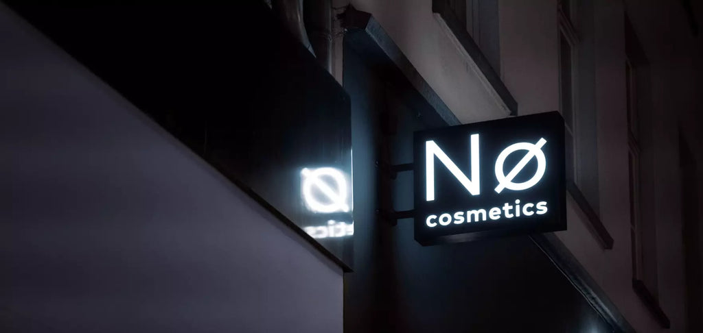 No Cosmetics double-sided projecting lightbox sign hanging on outside wall of flagship store on a dark street in Berlin