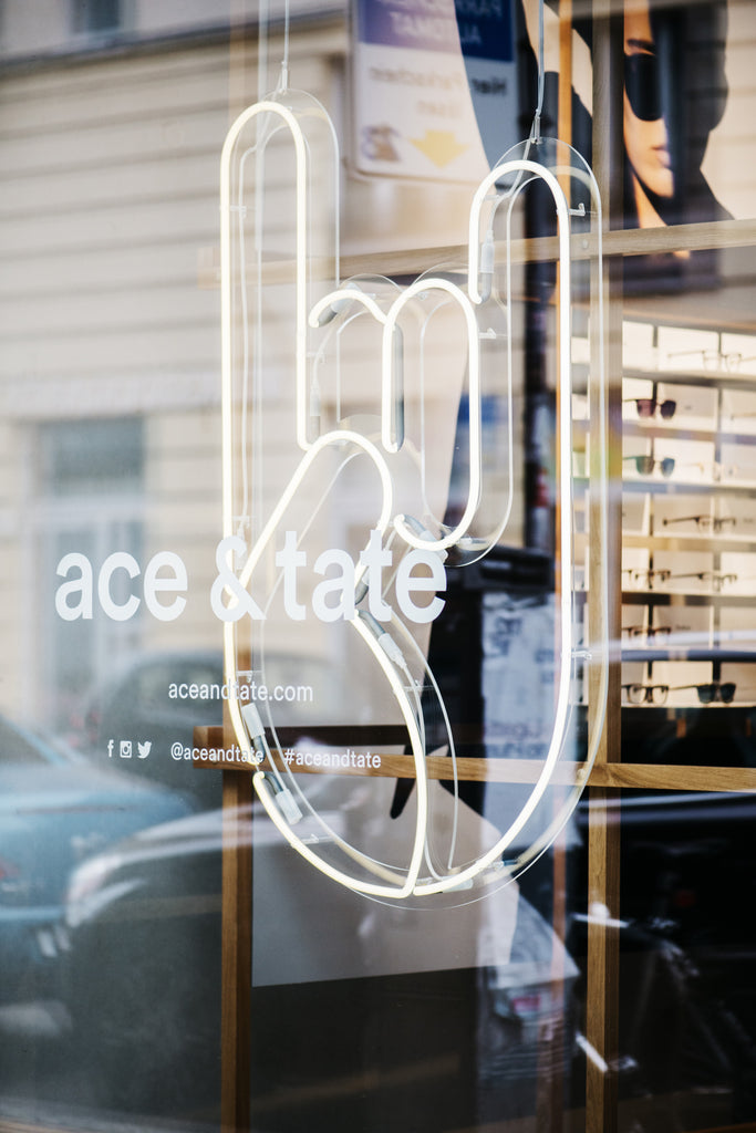 suspended glass neon sign in Ace & Tate storefront window