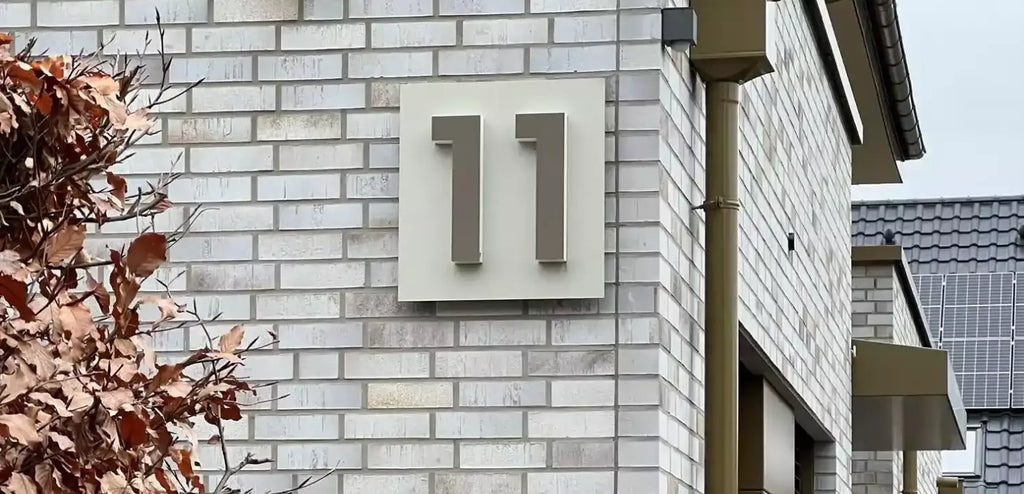 house number 11 eleven pre-mounted on a backplate mounted on a brick wall at daylight with the light turned off
