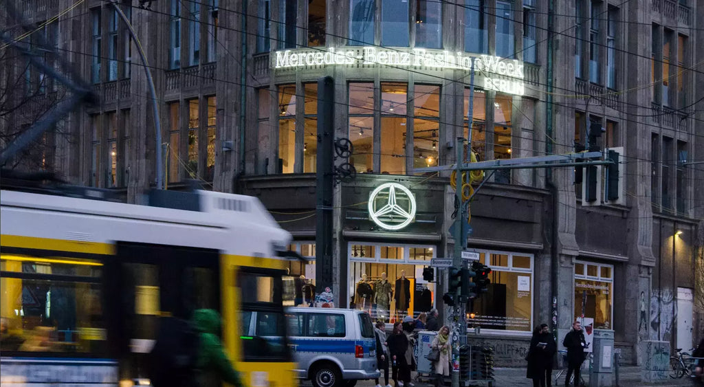 Berlin city scene with a bus, a police car, pedestrians, with a large Mercedes-Benz Fashion Week glass neon logo in the background